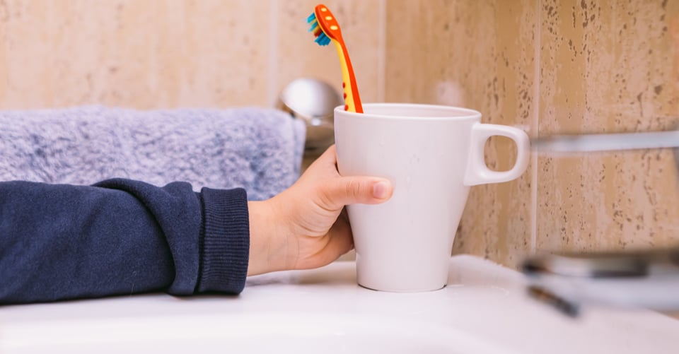 Child's hand holding cup with a device for brushing teeth
