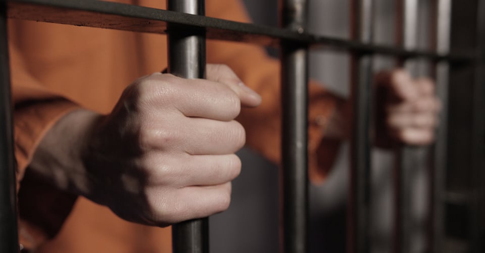 Manos de persona en barras de celda por cometer delito